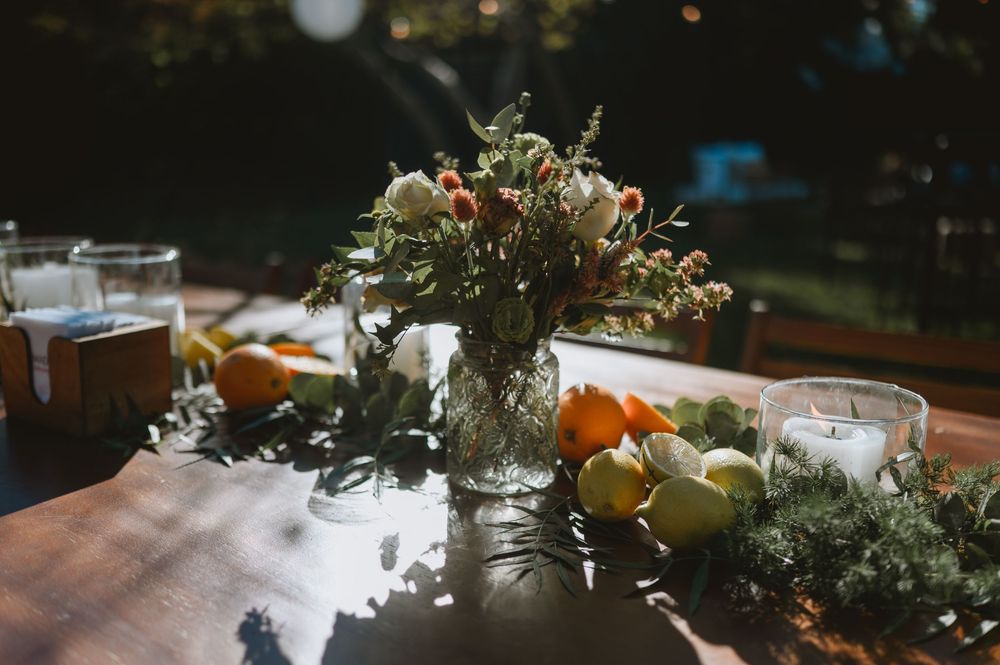 Rustic wedding table centerpiece featuring fresh flowers, citrus fruits, greenery garland, and white candles in glass holders.
