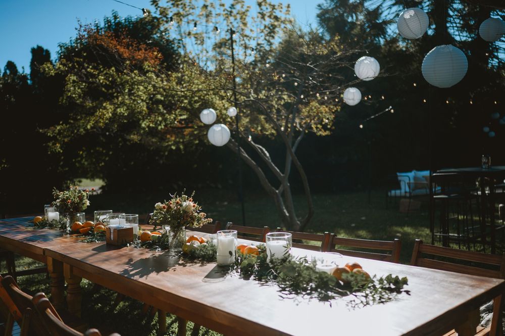 Outdoor wedding reception table with white paper lanterns, candle centerpieces, floral arrangements, and lush greenery backdrop.