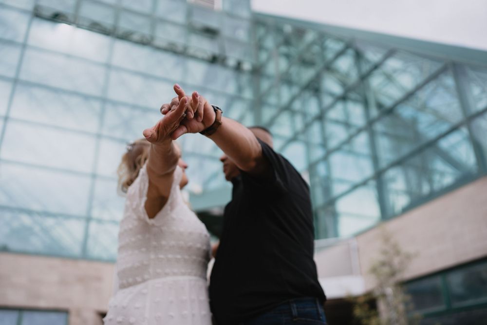 Couple dancing outdoors in front of a modern glass building, hands raised together in a joyful moment at Albuquerque Biopark