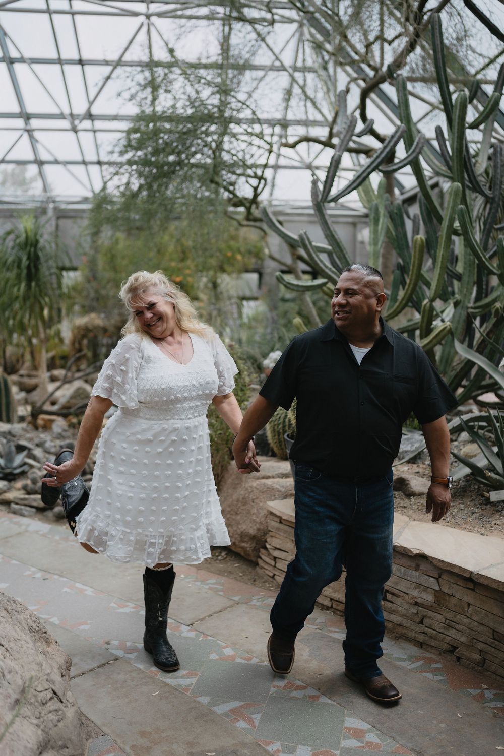 Couple holding hands and laughing while walking through a lush indoor cactus greenhouse at the Albuquerque Biopark