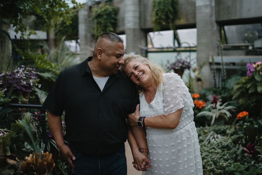 Happy couple embracing and smiling together surrounded by vibrant green plants in a greenhouse at the Albuquerque Biopark