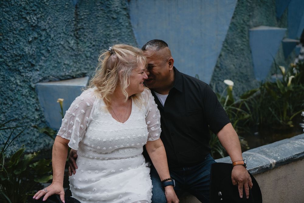 Couple sharing a tender moment seated against a blue textured wall in a botanical garden at Albuquerque Bio Park