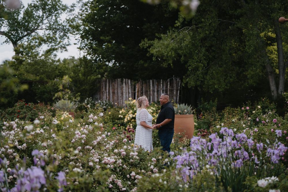 Couple holding hands and facing each other in a stunning garden filled with purple blooms at Albuquerque Bio Park