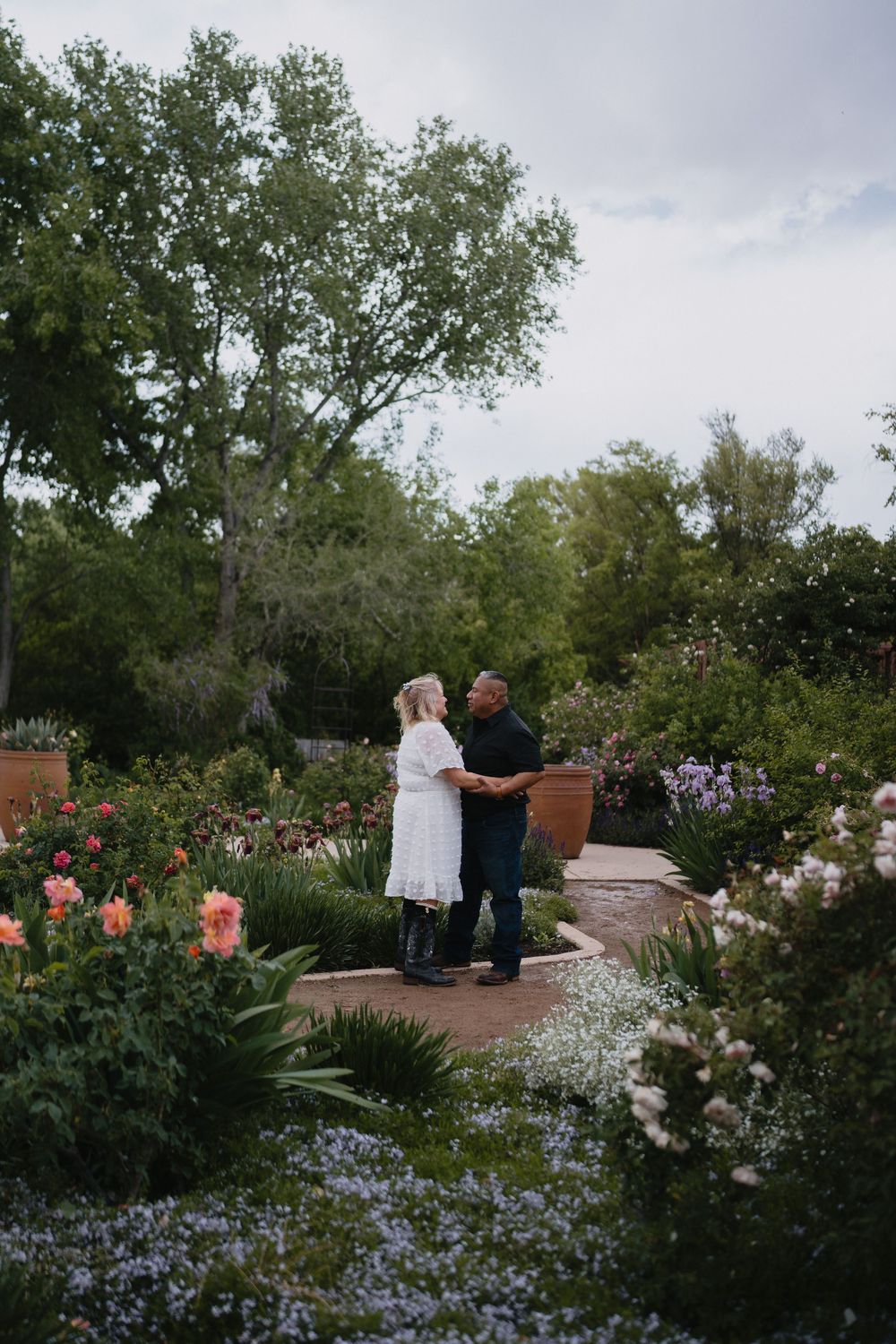 Couple dancing together on a garden path surrounded by colorful spring flowers and lush trees at Albuquerque Biopark