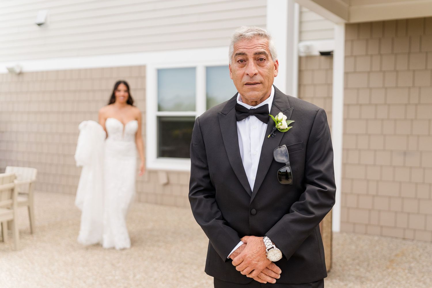 Man in tuxedo stands before bride in white gown during an outdoor wedding first look moment.