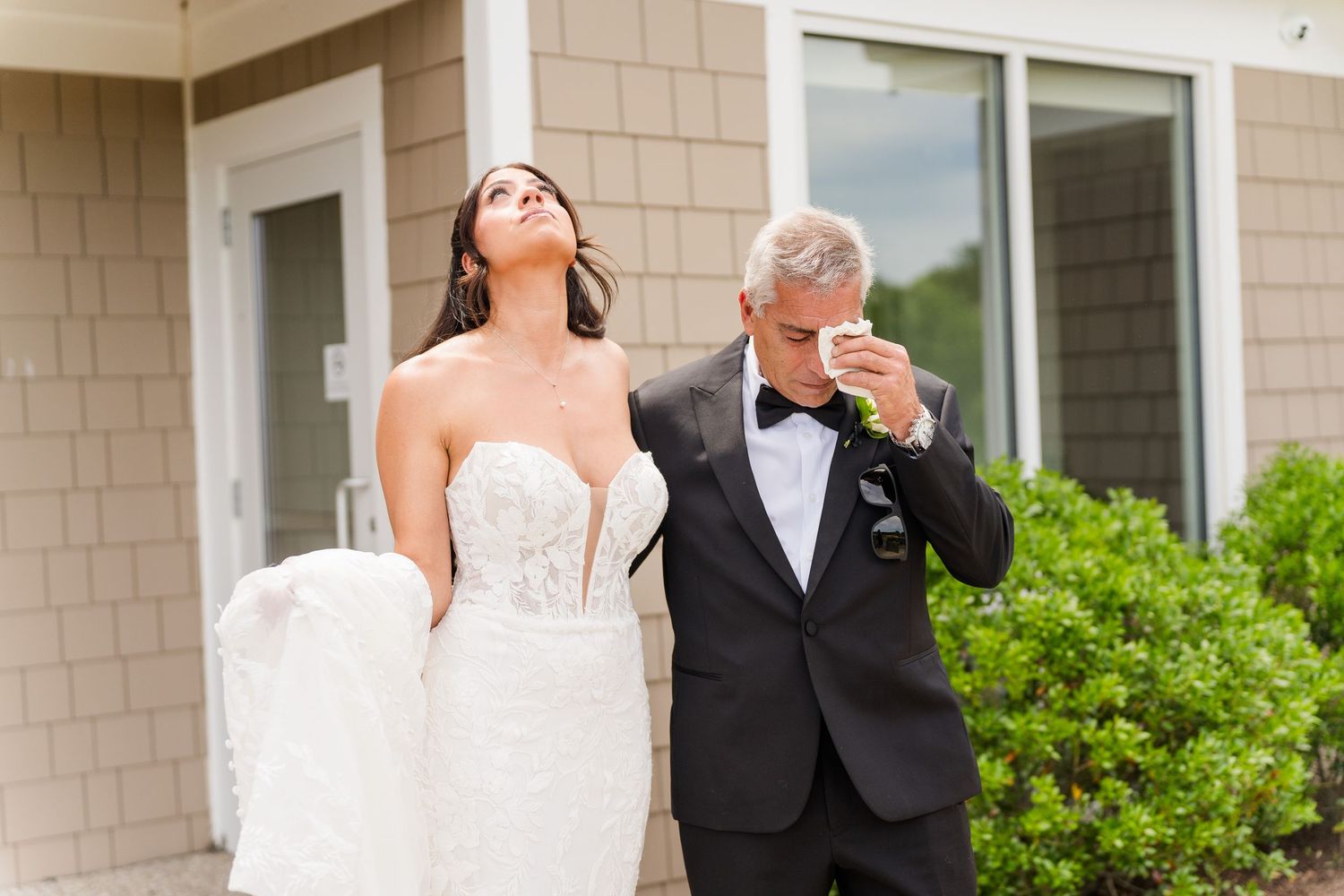 Emotional father wipes tears during first look with bride in strapless lace wedding gown.