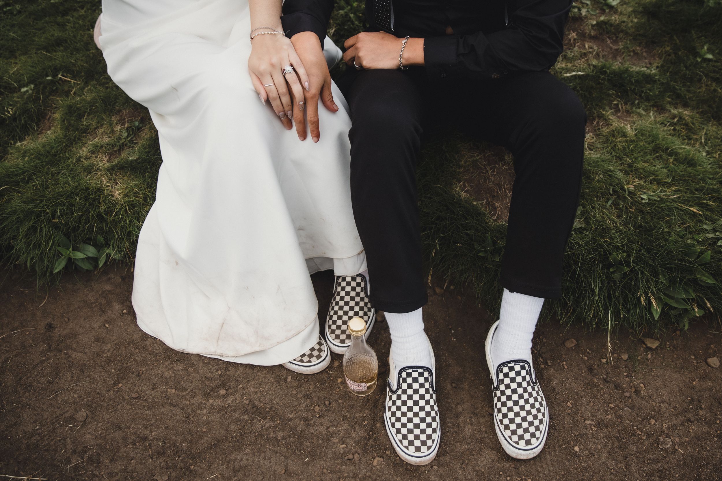 Couple in wedding attire wearing matching checkered Vans slip-on sneakers seated outdoors on their wedding day.