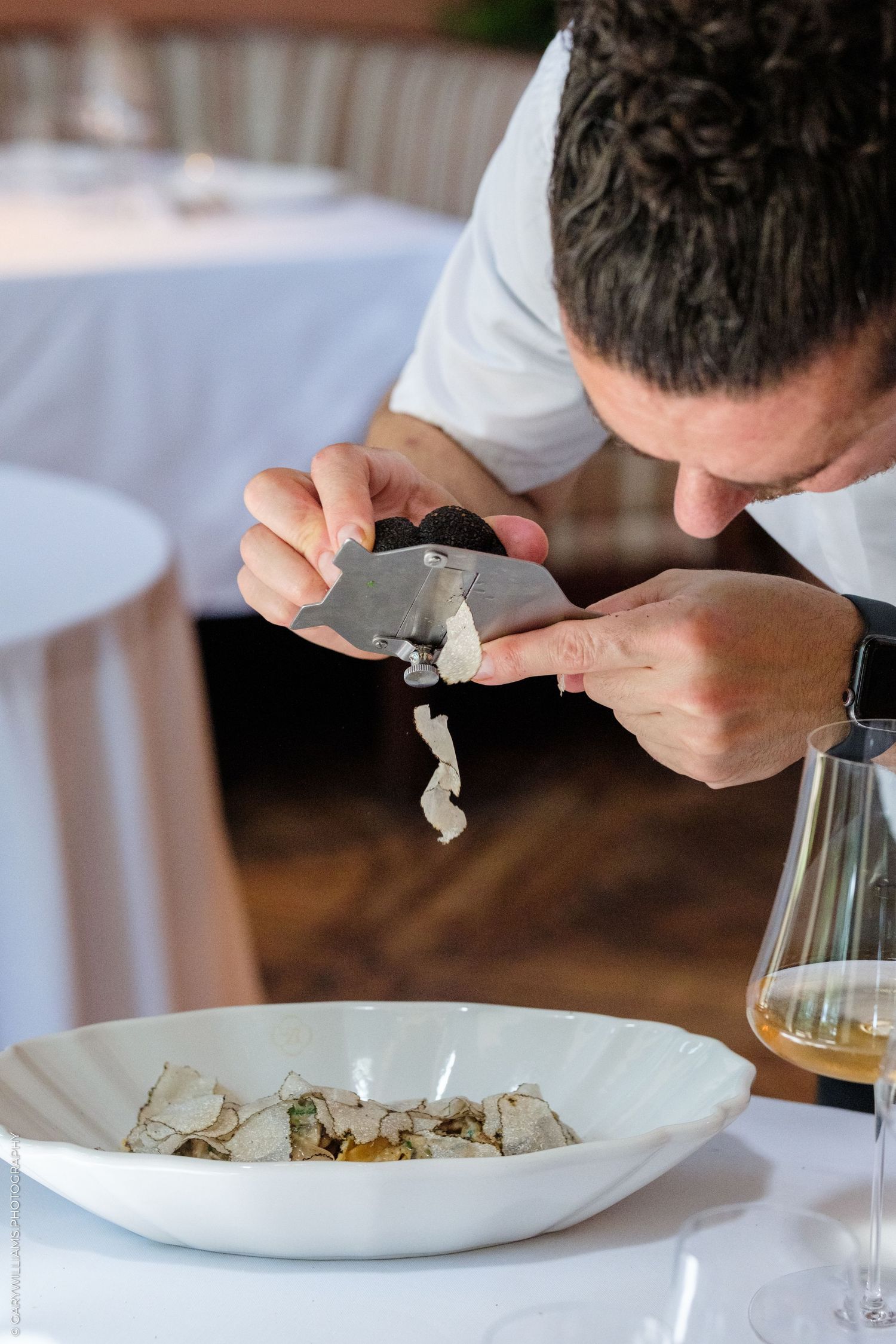 Chef shaving fresh truffle over a gourmet dish in a fine dining restaurant setting.