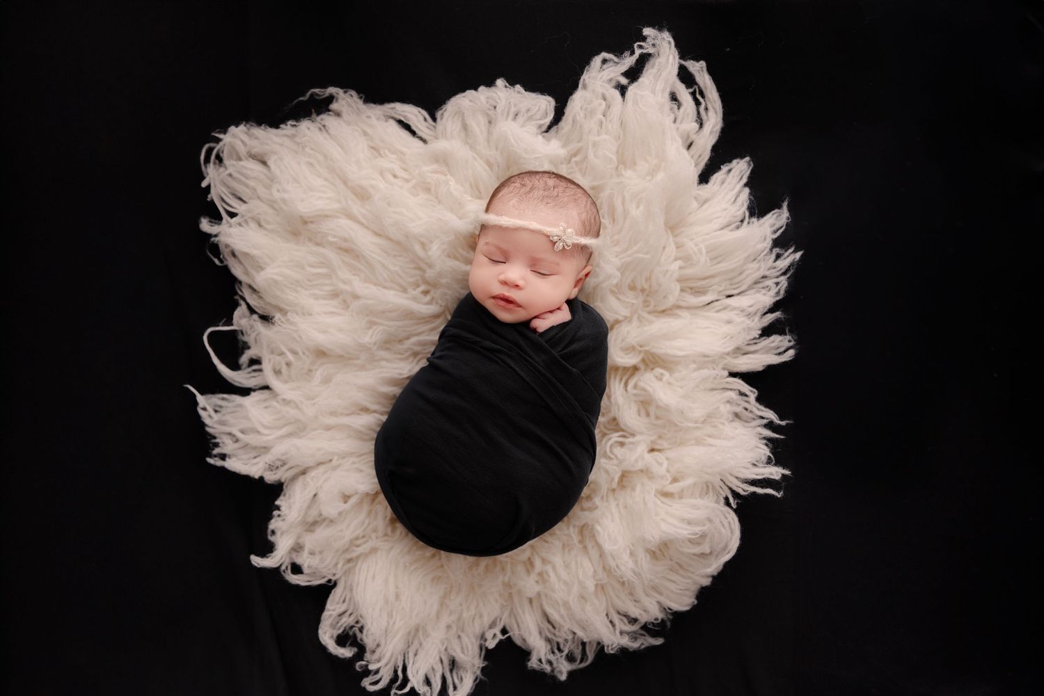 Peaceful newborn baby sleeping in black hat and wrap on dark background.