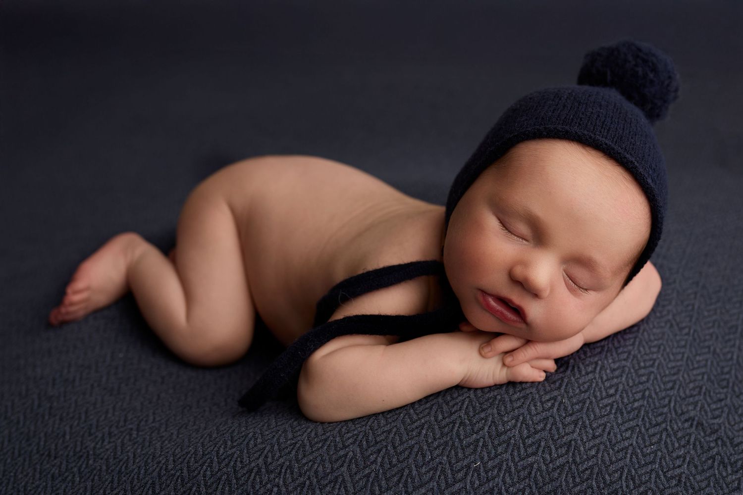 Sleeping newborn baby wrapped in blue knit swaddle with bonnet, nestled in a light blue box on a blue background.