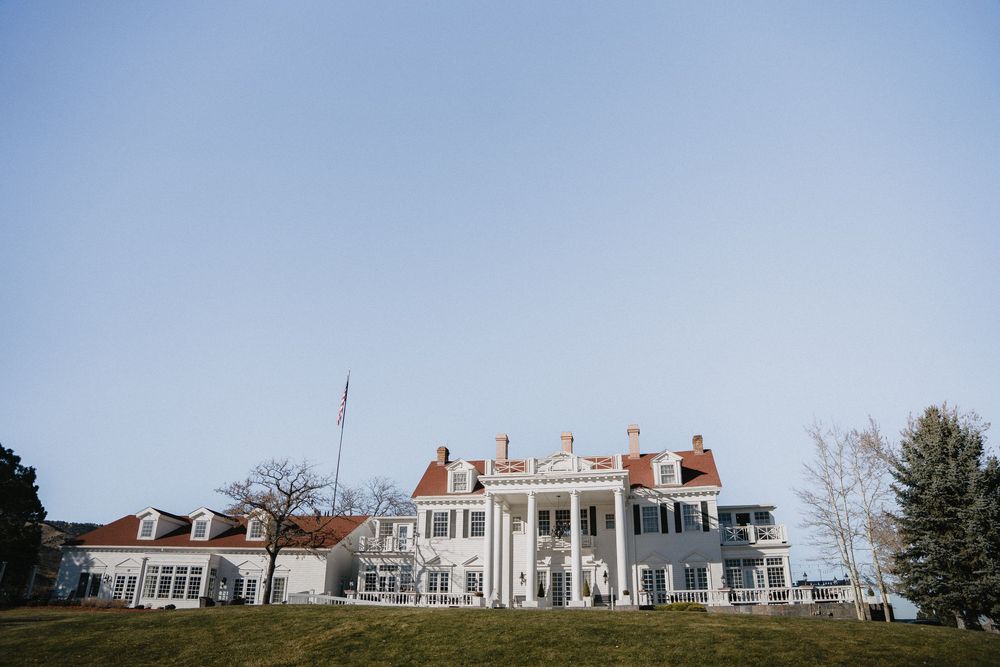 Grand white colonial mansion with red roof, columns, and manicured lawn under clear blue sky.