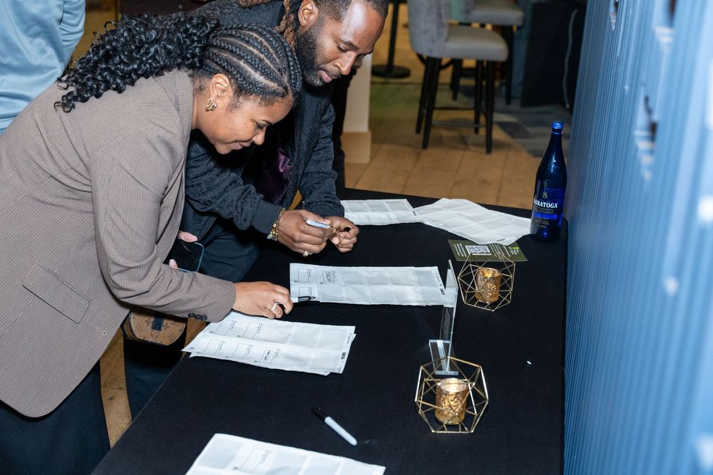 Two people signing documents at a black table during a formal event with decorative gold geometric candle holders.