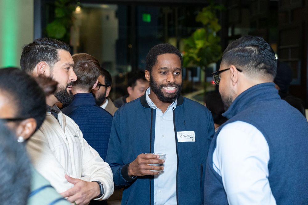 Diverse group of professionals networking at an indoor corporate event, smiling and engaging in conversation.