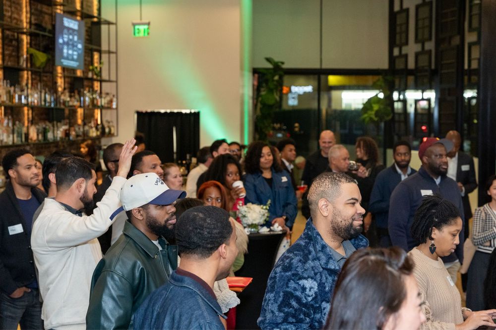 Diverse crowd of professionals networking at an indoor event venue with green ambient lighting.