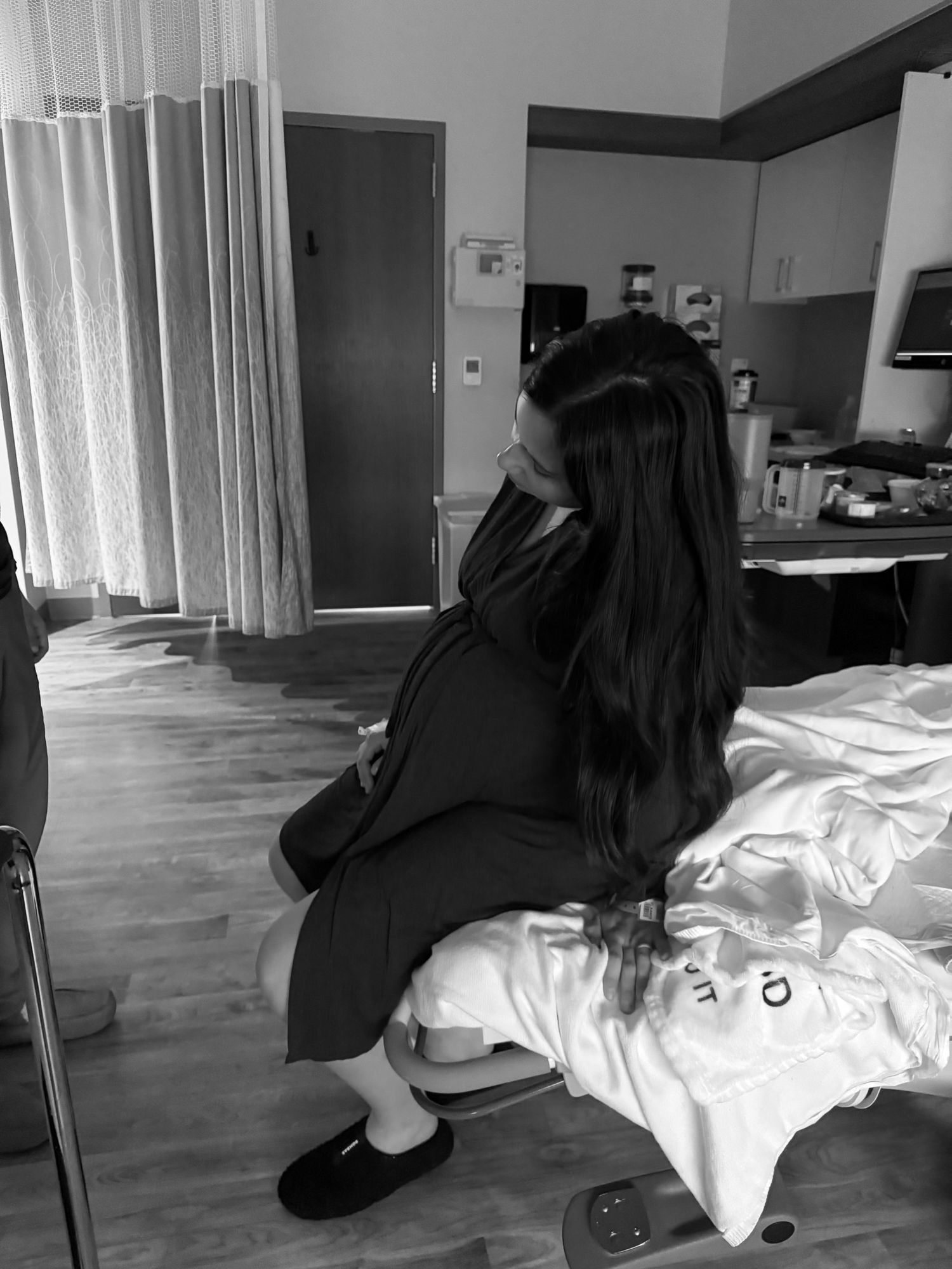 Pregnant woman sitting on hospital bed in black and white photo.