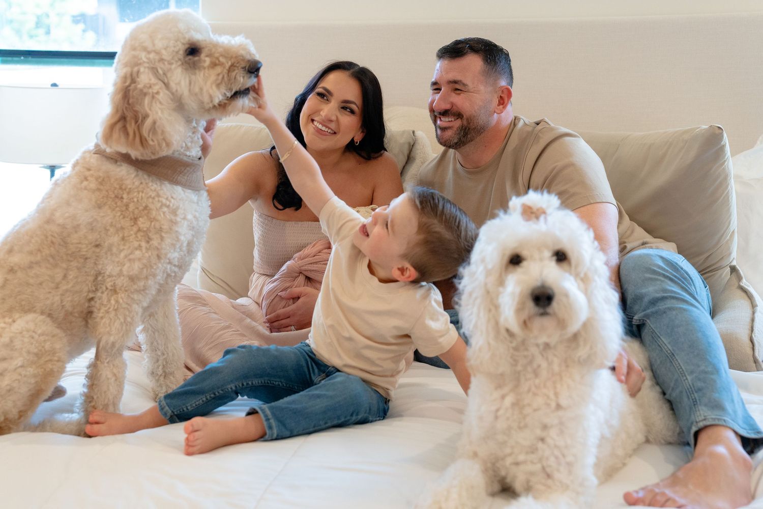 Family with two white Goldendoodles sitting in a pink nursery with a crib and Riley name sign on the wall.