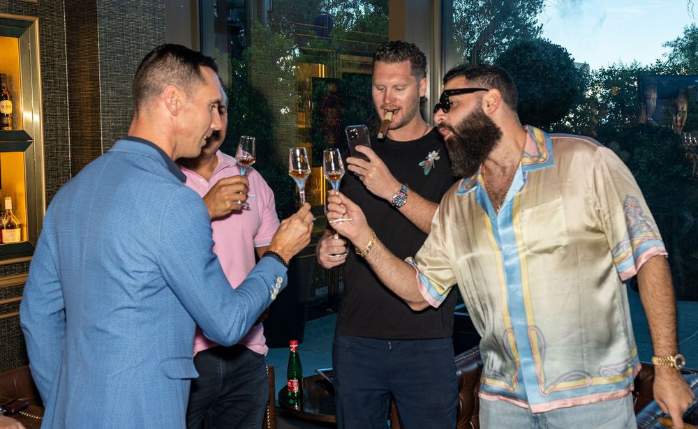 Four men toasting with champagne glasses at an elegant outdoor evening social gathering.