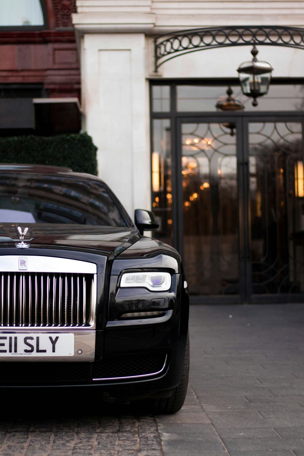 Black Rolls-Royce Ghost with license plate E11 SLY parked outside a luxury hotel entrance.