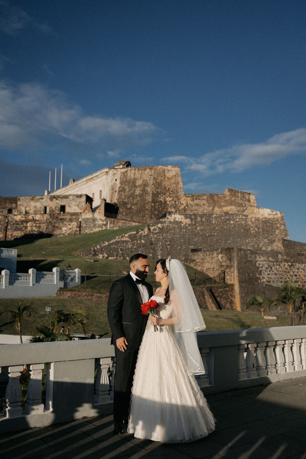 Bride and groom pose romantically on a terrace with historic El Morro fortress backdrop in Old San Juan, Puerto Rico.