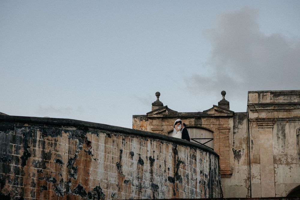 A person in white dress stands atop an ancient stone fortress wall under a cloudy sky.