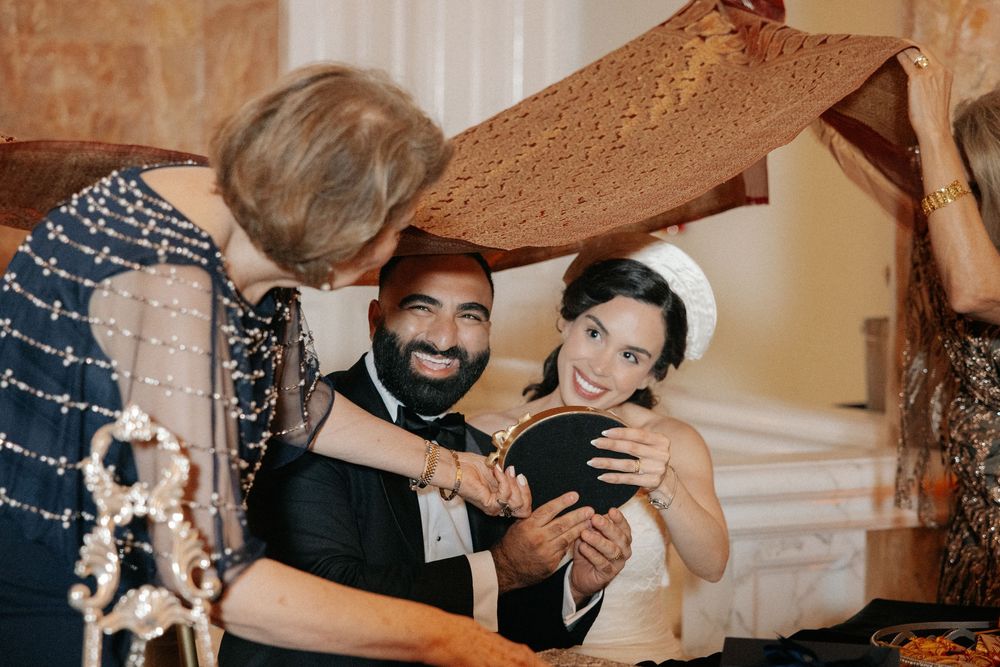 Bride and groom smiling under a traditional Jewish chuppah cloth during their wedding ceremony.
