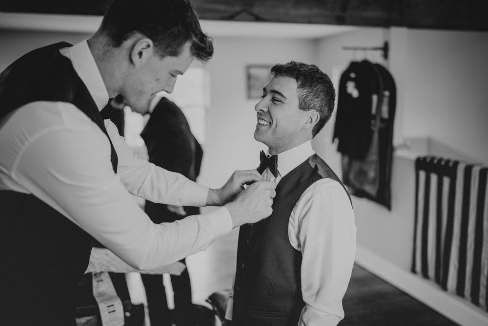 Black and white photo of two groomsmen adjusting bow ties while getting ready for a wedding ceremony.
