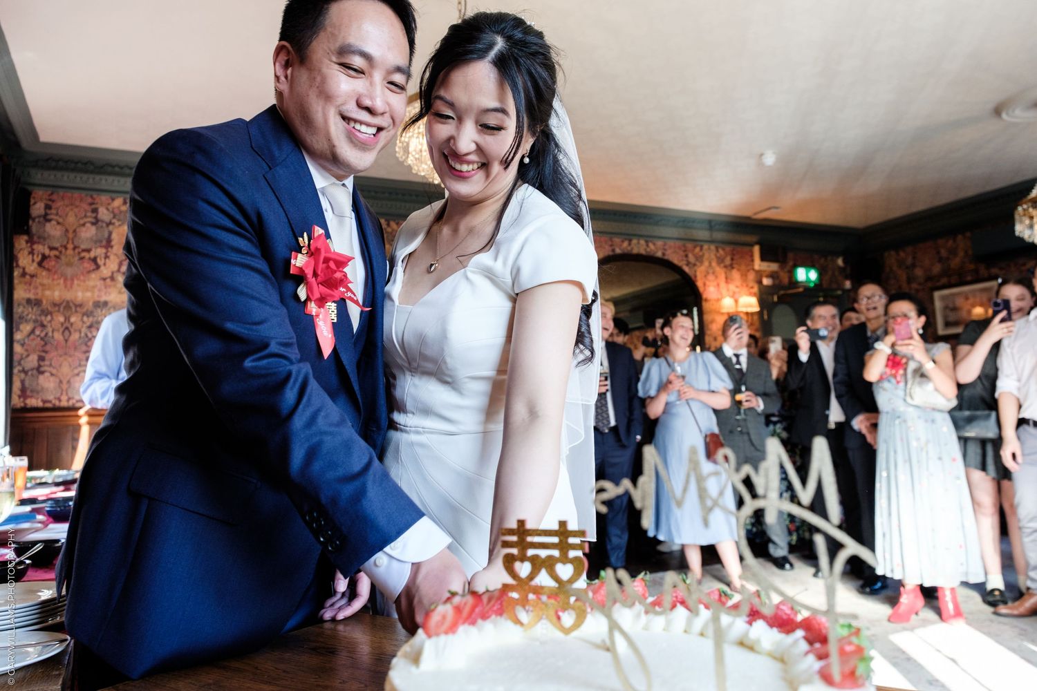 Asian bride and groom cutting wedding cake together at reception.