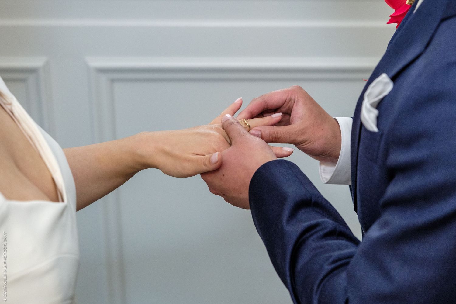 A groom in a navy suit places a wedding ring on the bride's finger during a ceremony.