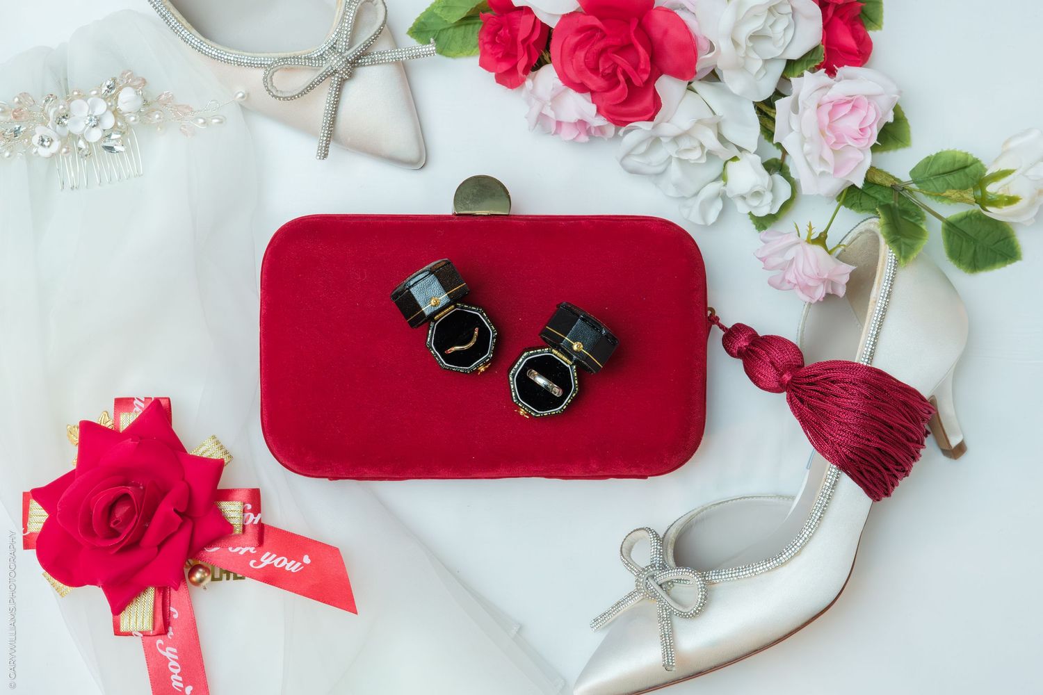 Red velvet clutch with wedding rings, roses, and bridal accessories arranged elegantly.