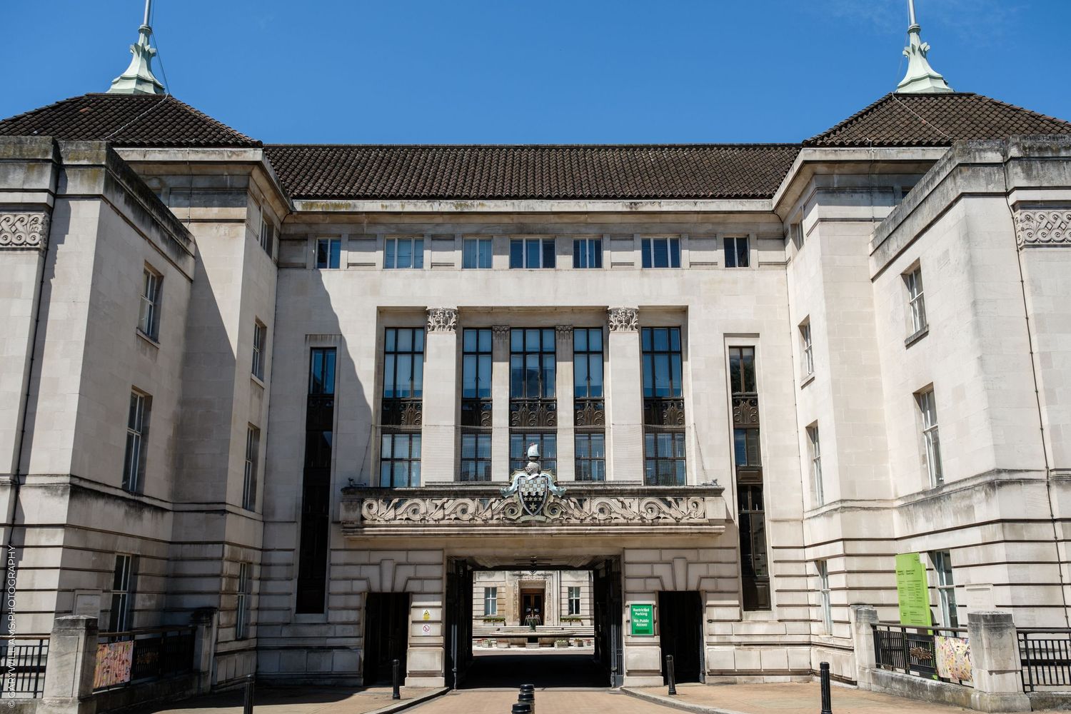 Grand neoclassical government building facade with white stone columns and ornate entrance archway under clear blue sky.