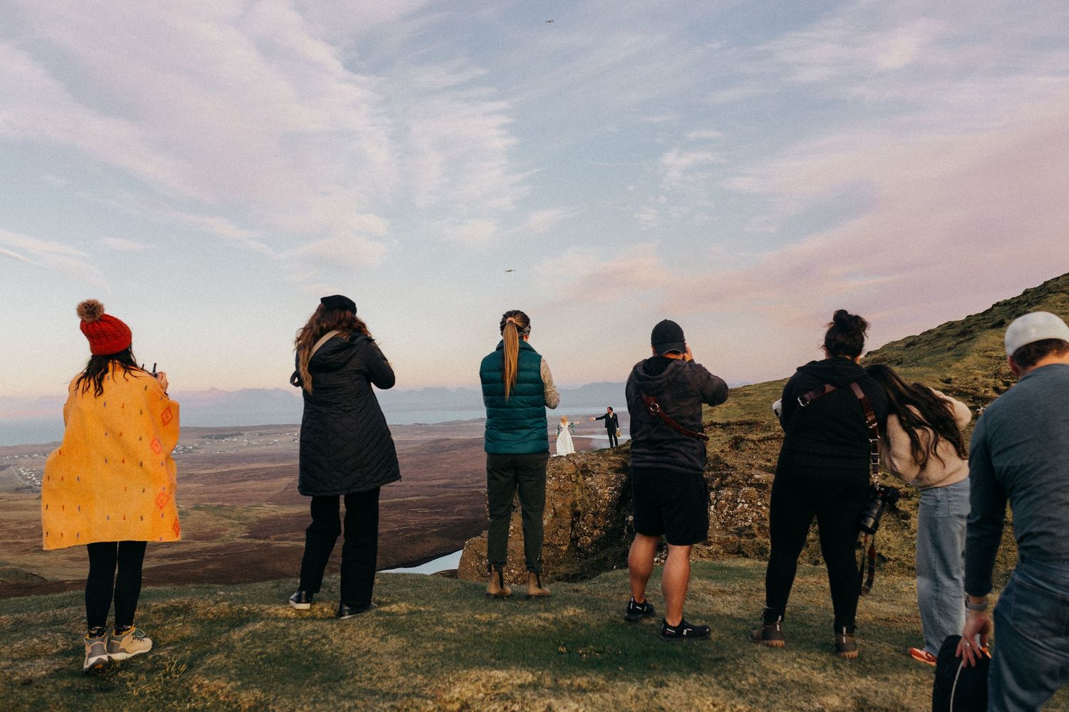 Group of hikers standing on a mountain summit at sunset, enjoying panoramic views of a vast landscape below.