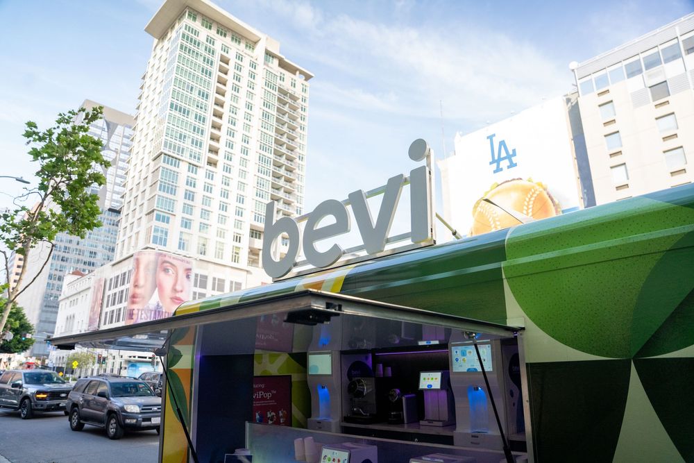 Bevi branded outdoor kiosk on a city street with colorful geometric design and urban buildings in the background.