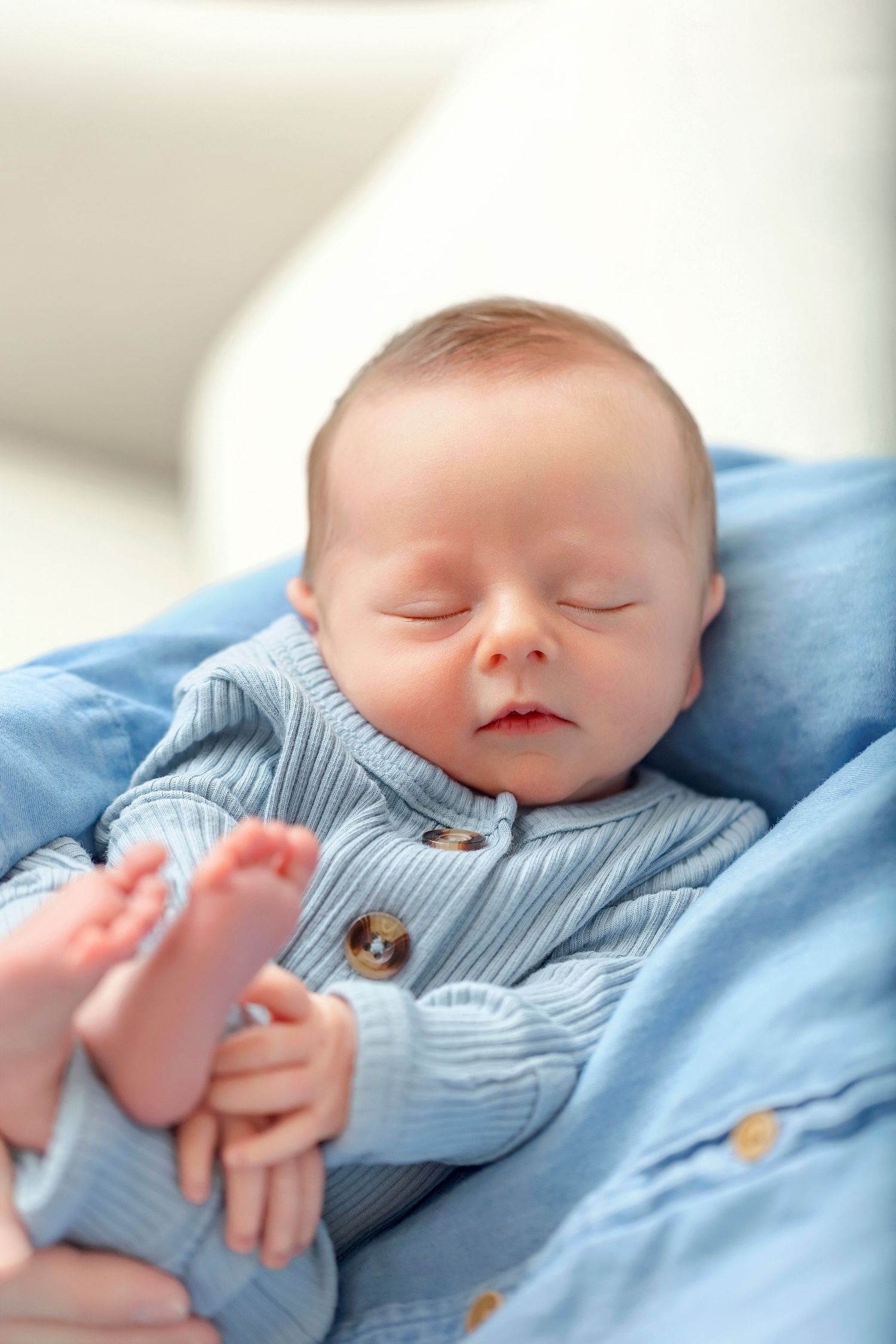 Close-up portrait of a sleeping newborn baby boy in blue knit clothing.