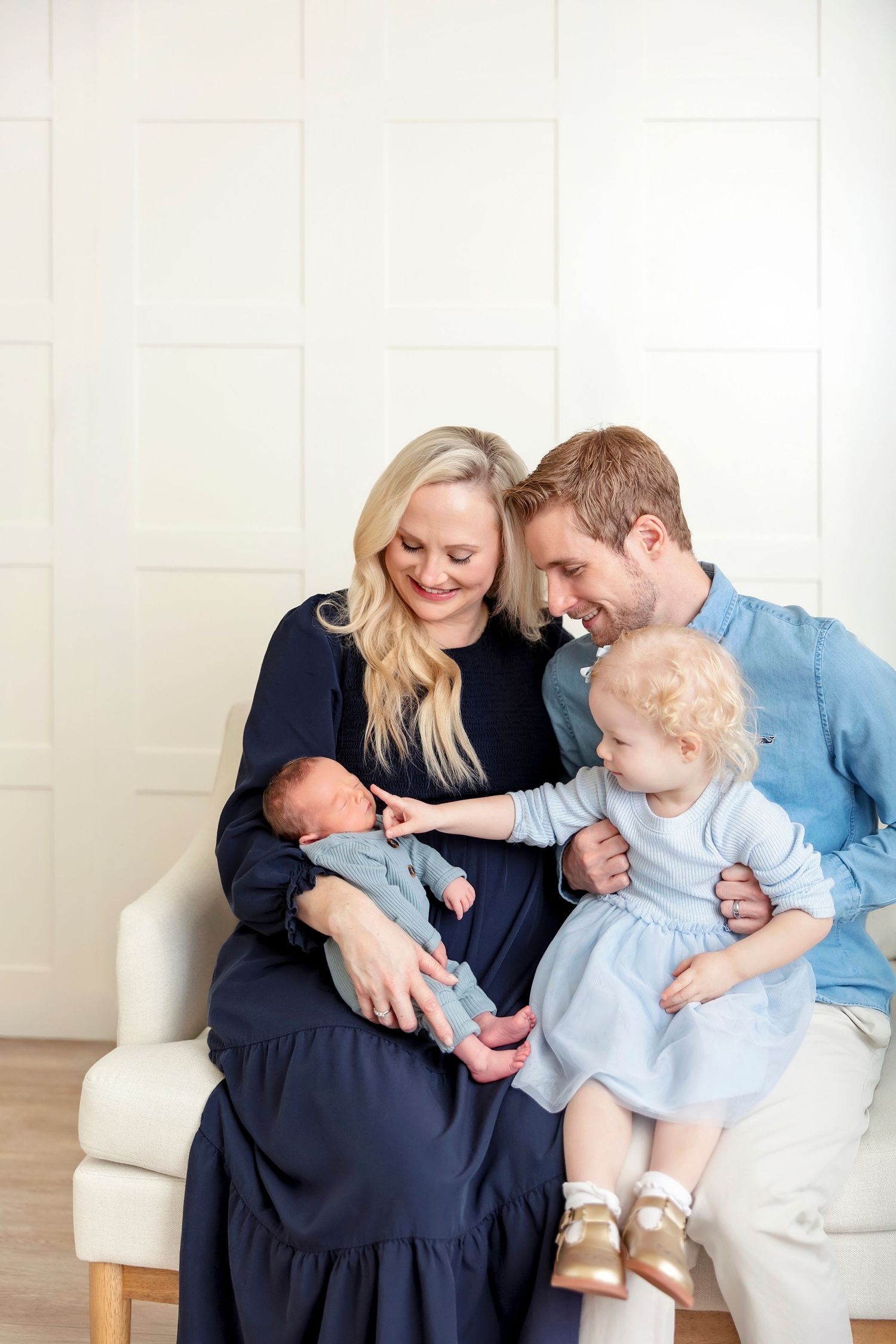 Parents cuddling their newborn son with big sister during a studio newborn photography session.