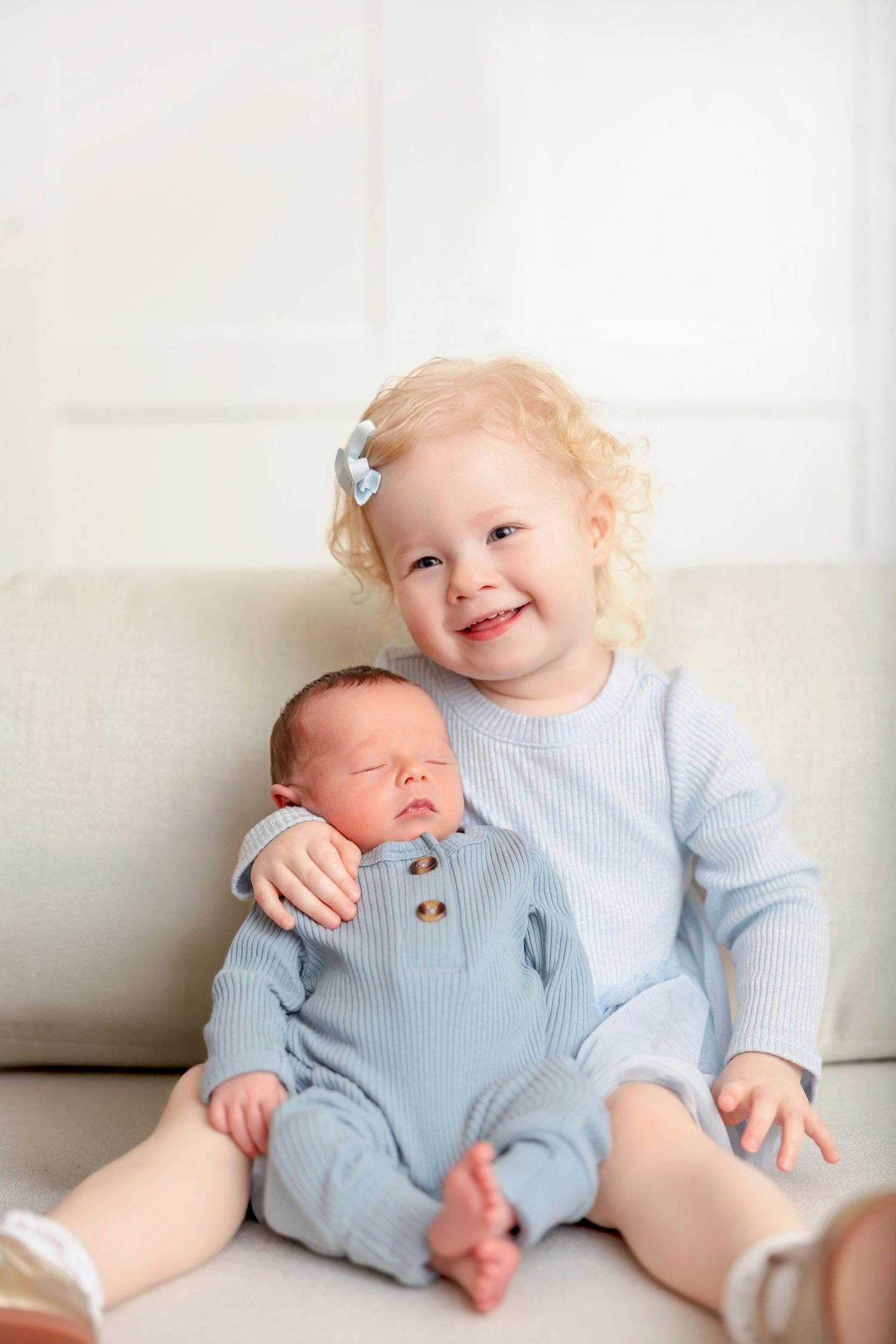 Big sister smiling while holding her newborn baby brother during a studio newborn session.