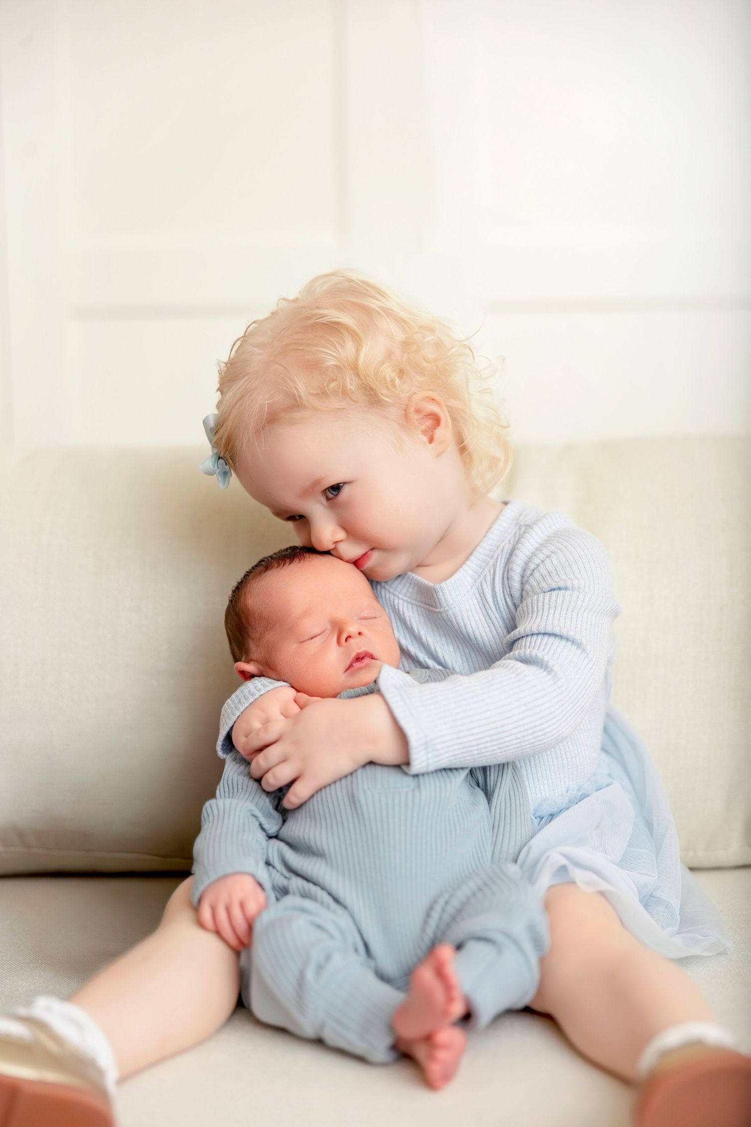 Sweet sibling portrait of a toddler hugging her sleeping newborn baby brother.