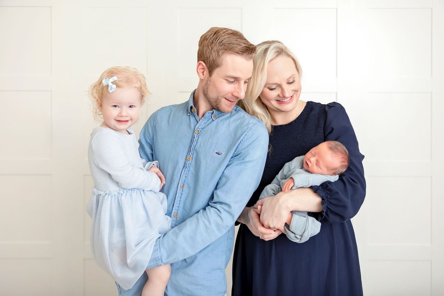 Family of four embracing during a timeless studio newborn photography session.