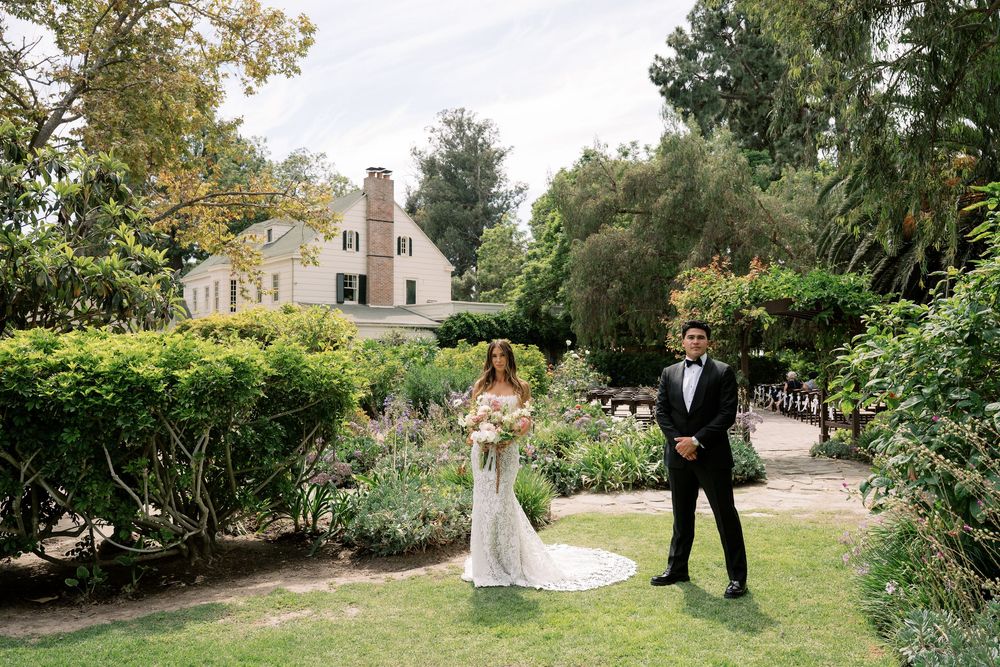 Bride and groom stand in lush garden grounds of elegant estate venue on their wedding day.