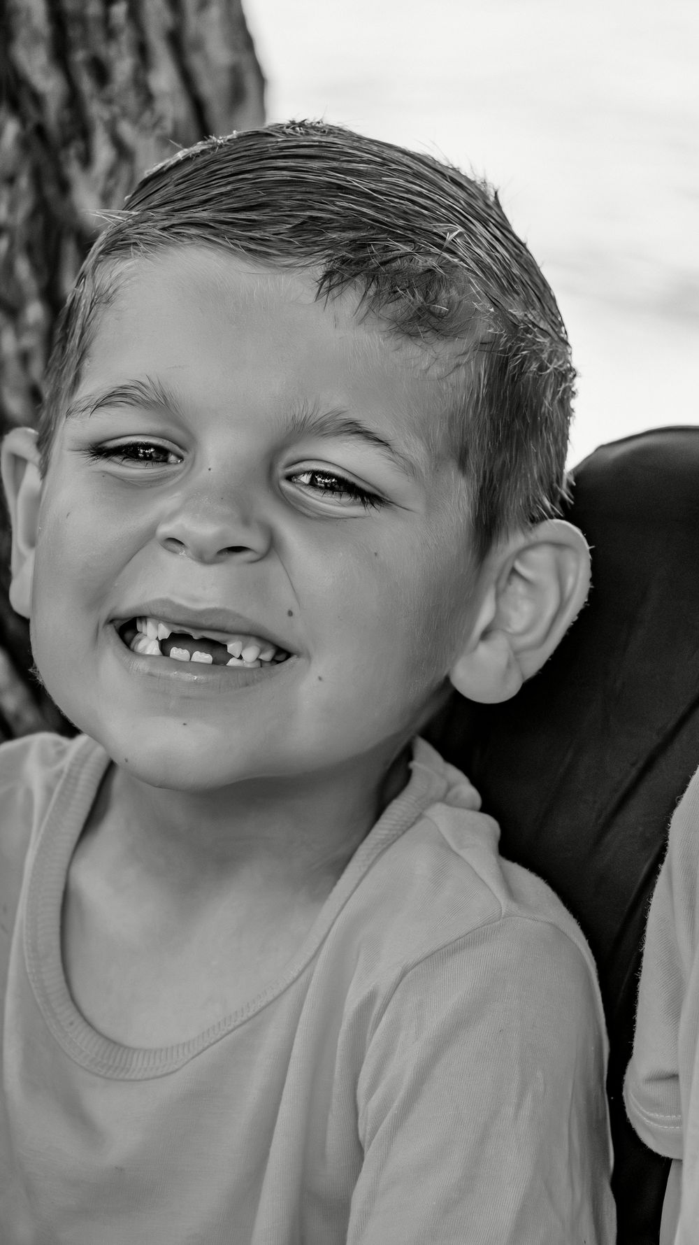 A cheerful young boy with a gap-toothed smile poses for a black and white portrait photograph.