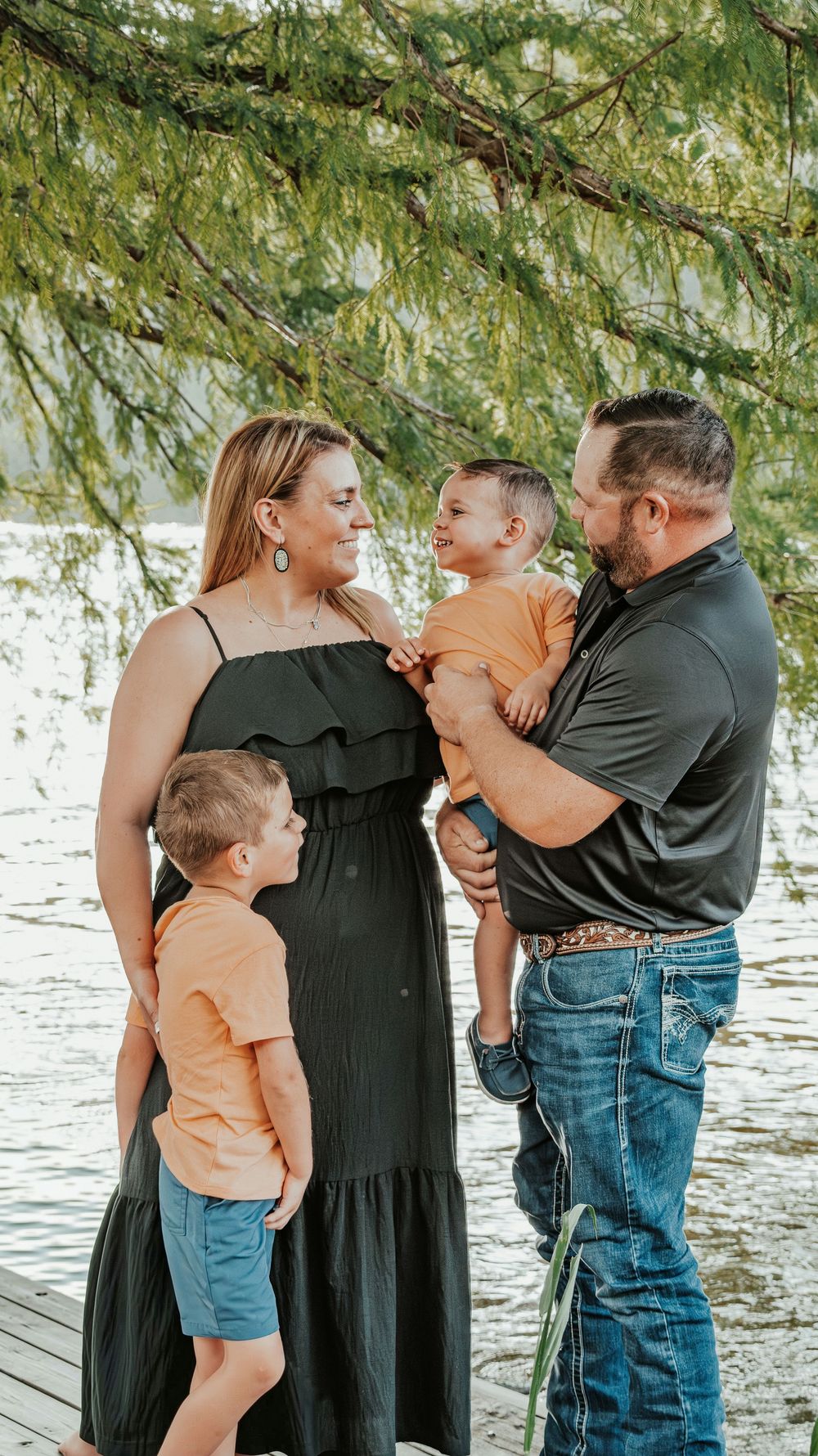 A loving family of four poses on a lakeside dock, with two boys in orange shirts and their parents.