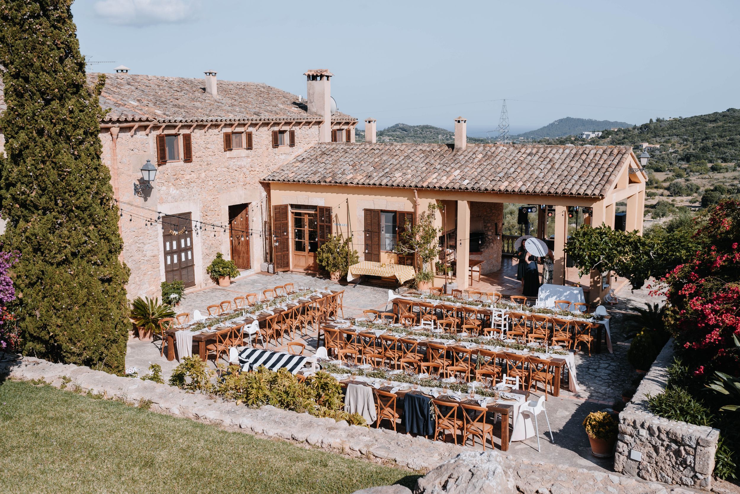 Mediterranean villa with rustic outdoor dining setup featuring wooden tables and chairs arranged on a stone terrace.