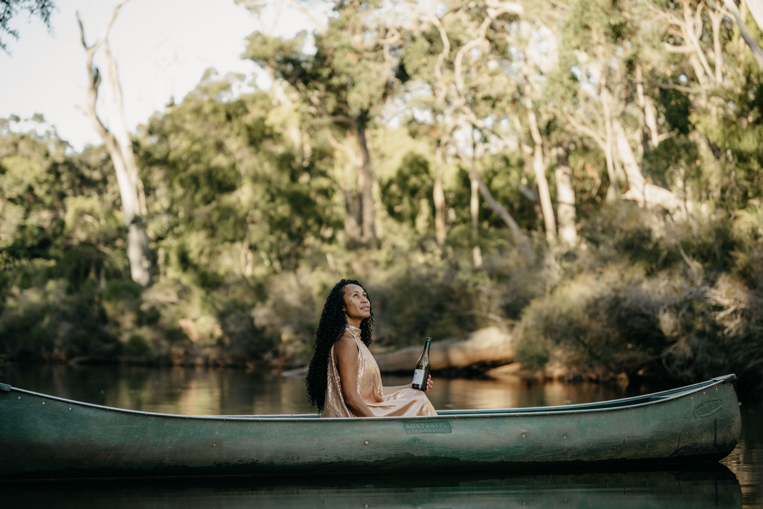 A young woman sits peacefully in a canoe on a calm river surrounded by eucalyptus trees.