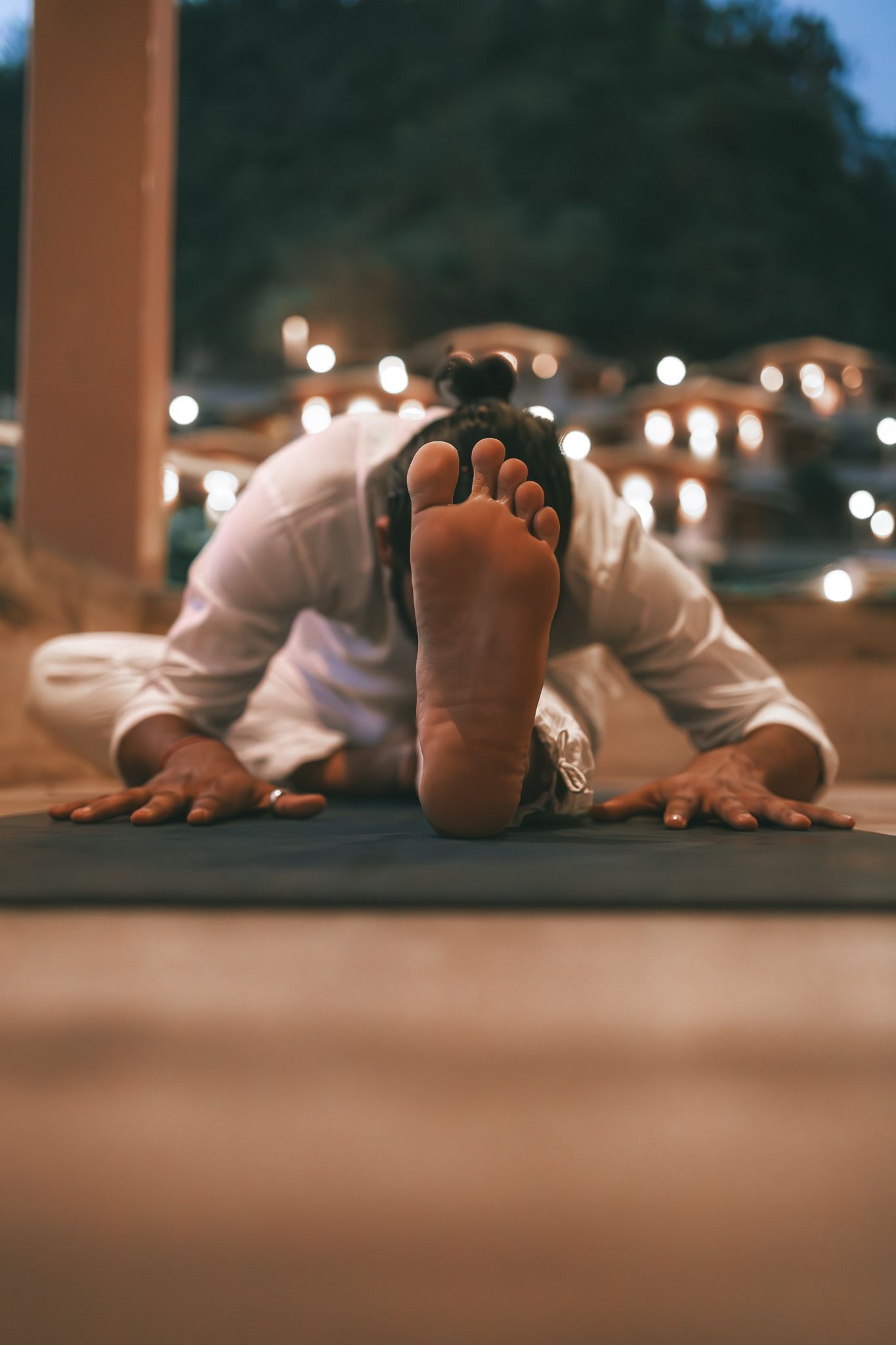 Person performing child's pose yoga stretch on mat outdoors at night with bokeh lights in background.