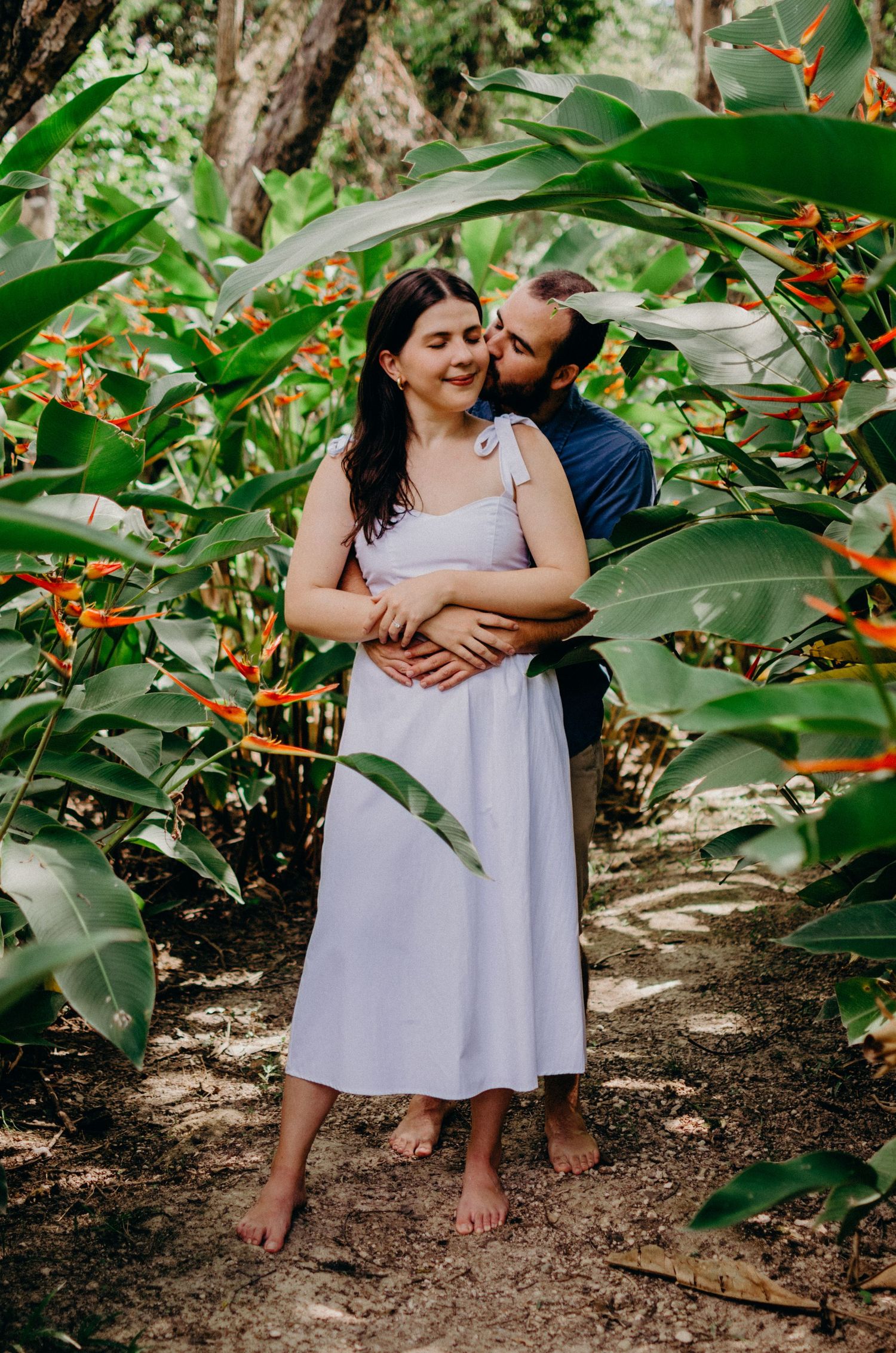 Romantic couple embracing among tropical plants and flowers in a garden setting.