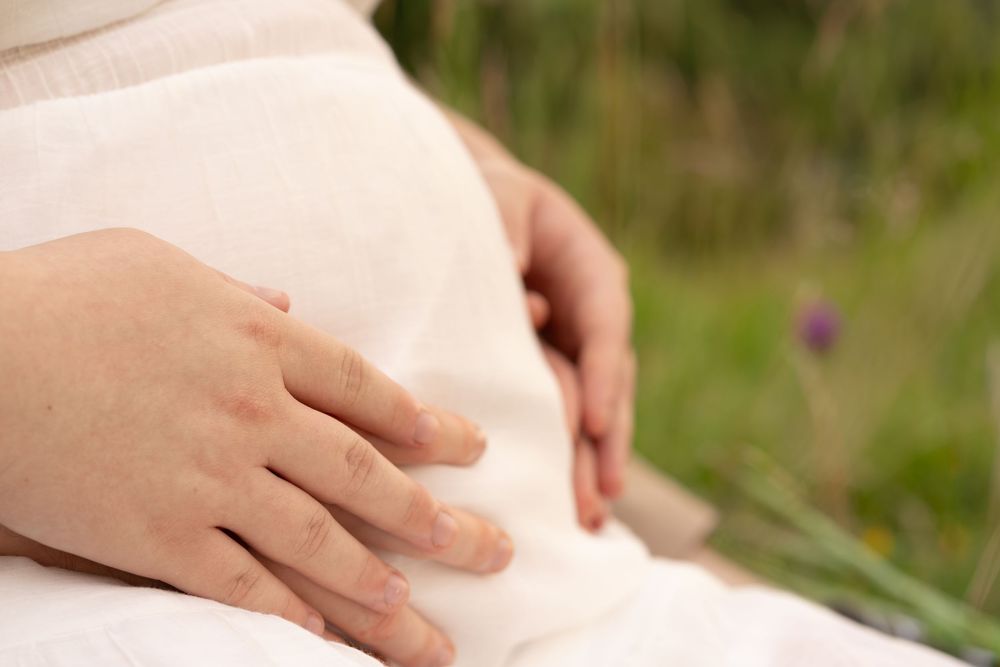 Close-up of pregnant woman gently cradling her baby bump outdoors in a lush green natural setting.