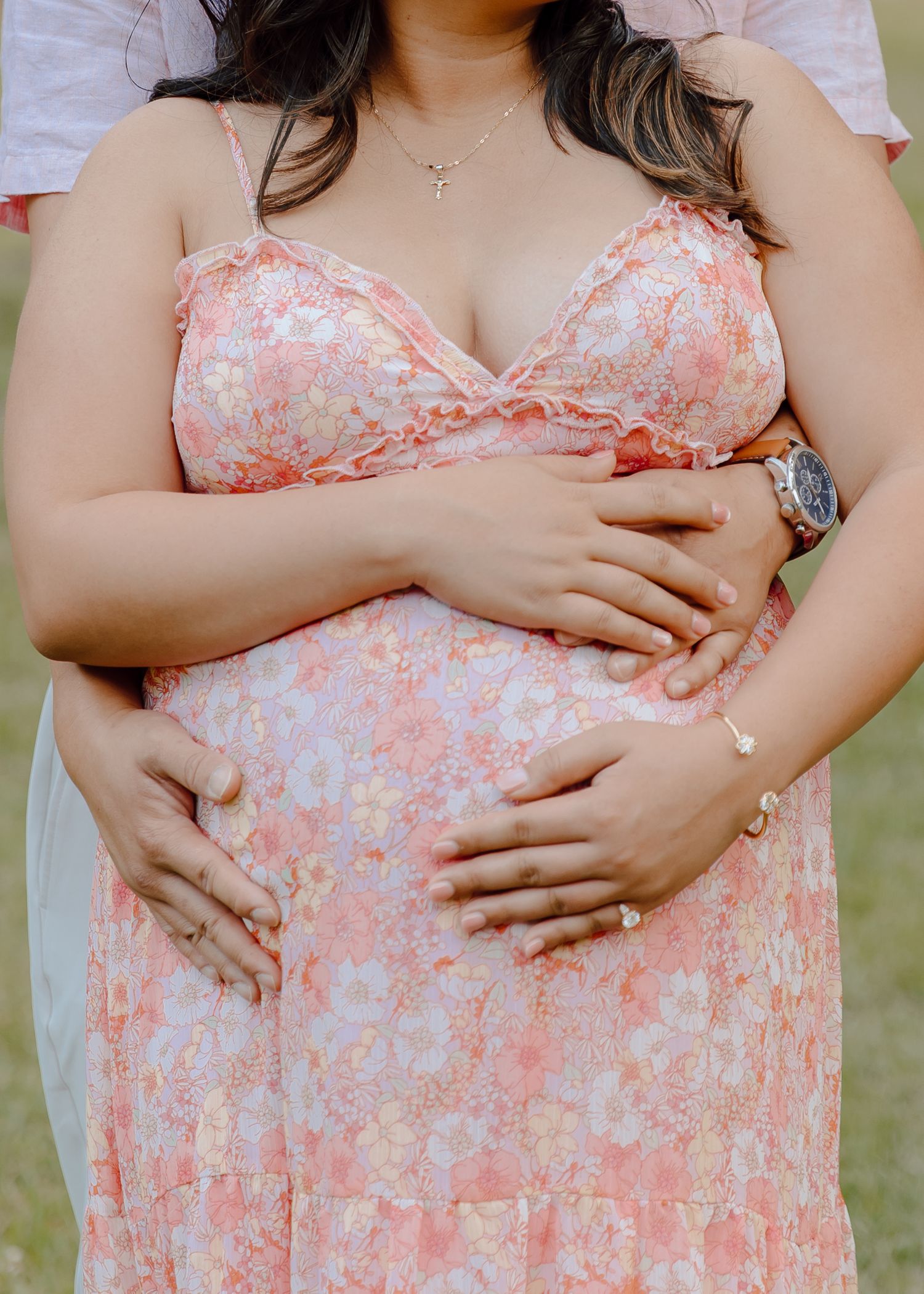 Pregnant woman in pink lace gown sits on grass under Spanish moss-draped oak trees during maternity photoshoot.