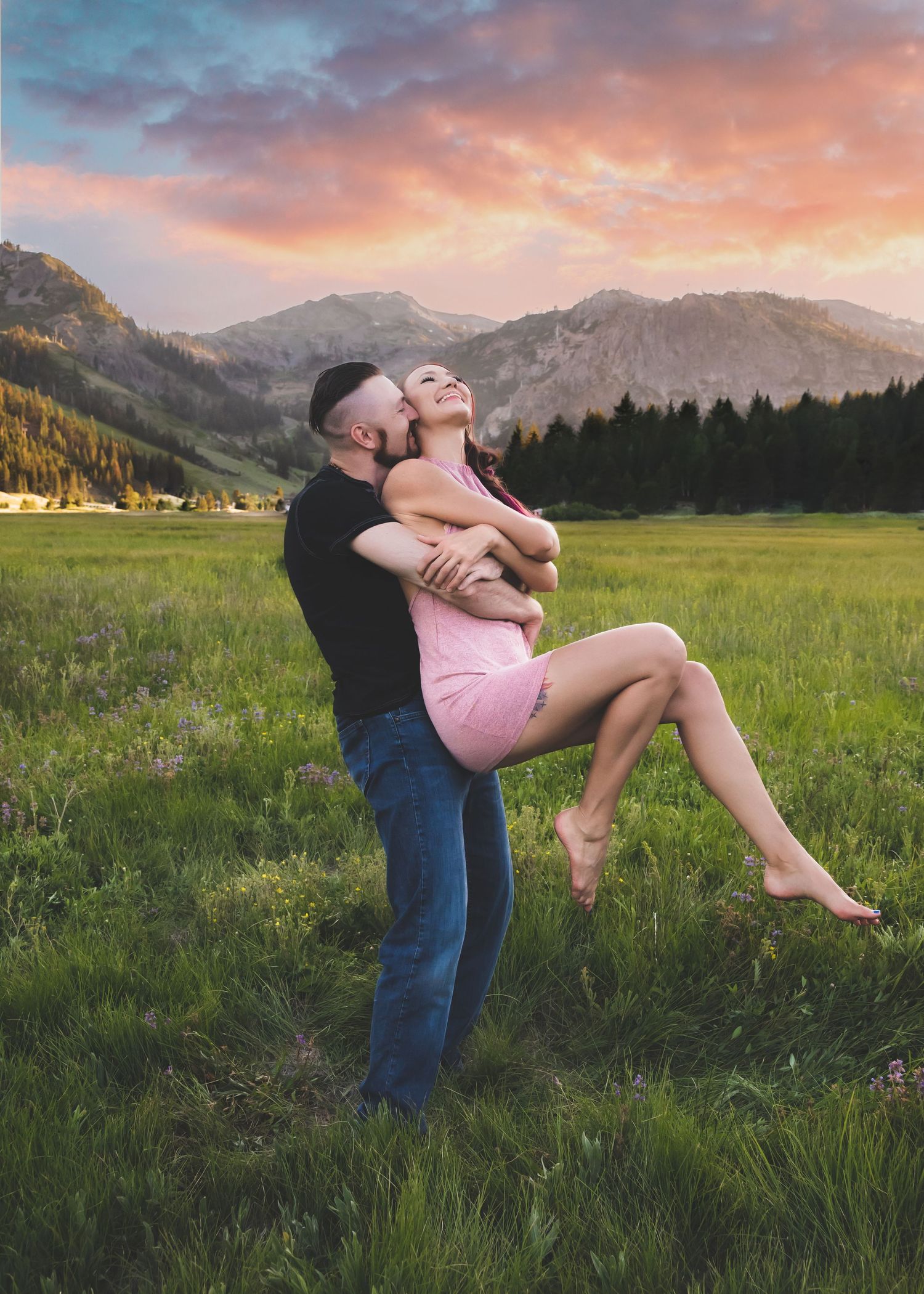 Couple embracing in mountain meadow at sunset with colorful sky.