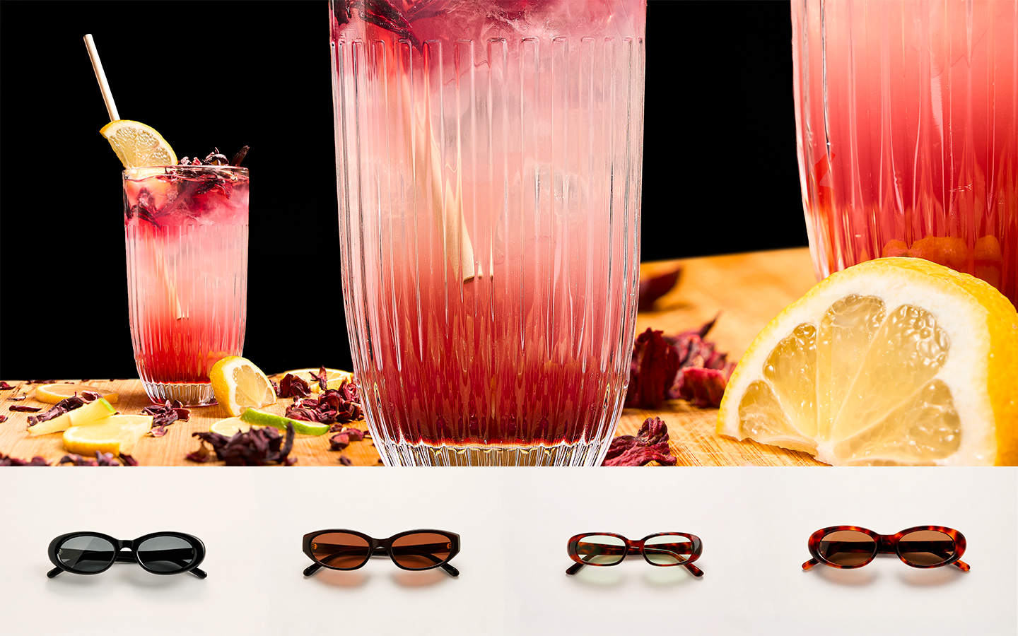 Stylish sunglasses collection displayed in front of vibrant red cocktail drinks with lemon and dried flowers.