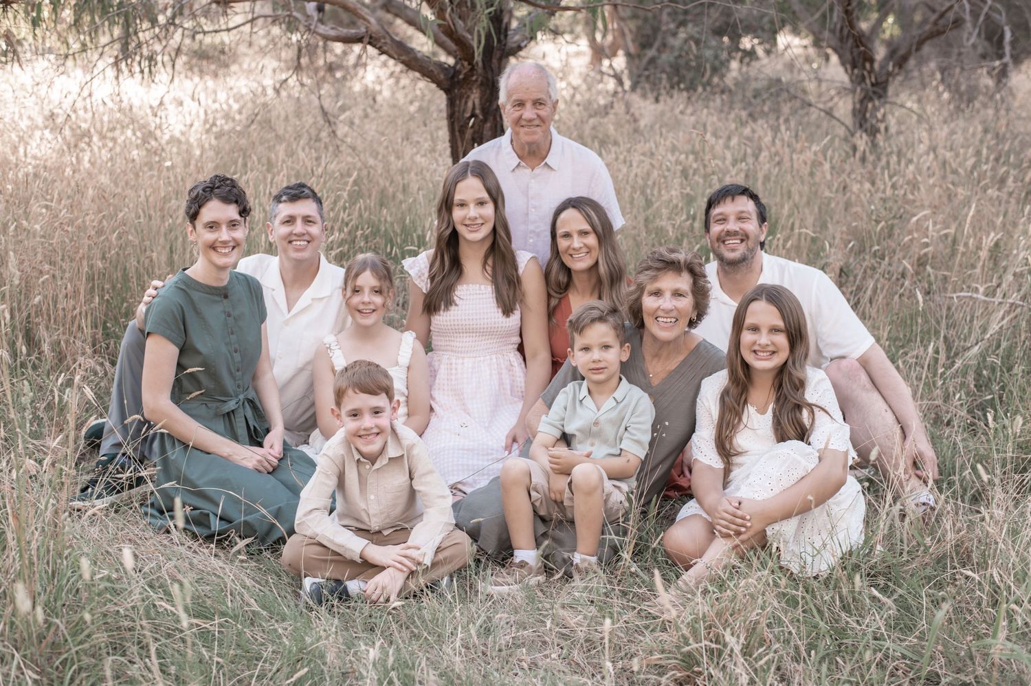 Large family group portrait outdoors in a golden field with eucalyptus trees, wearing soft neutral and earthy tones.