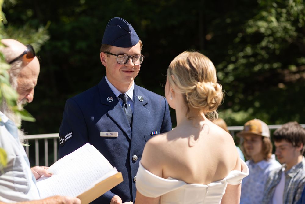 Air Force officer in dress uniform speaks with woman in white off-shoulder dress at outdoor ceremony.